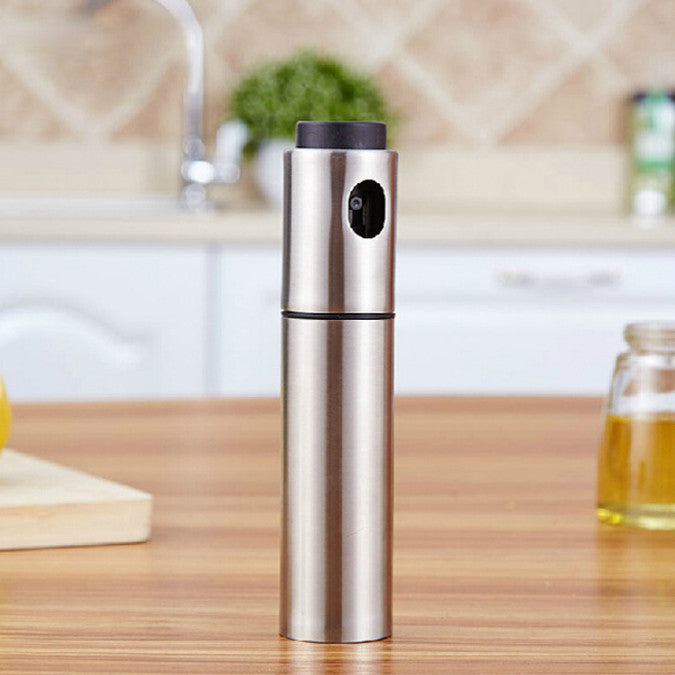 The Mr. Mister Point And Spray Olive Oil Spritzer by VistaShops stands on a wooden kitchen counter with a blurred background, making it the perfect healthy cooking tool for your modern kitchen.